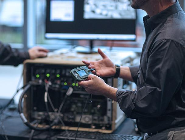 关闭-up of of a man in a lab, talking to ano的r hg皇冠官网 employee, holding a piece of 卫星通信 equipment