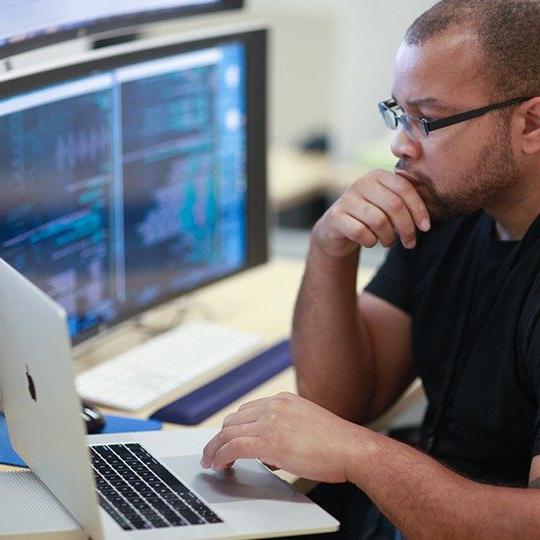 Viasat employee working at a laptop on managed network services next to a larger monitor